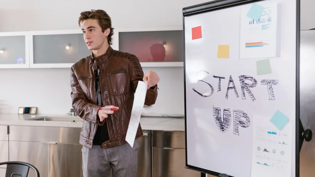 Une personne présente des documents devant un tableau portant la mention Start Up.